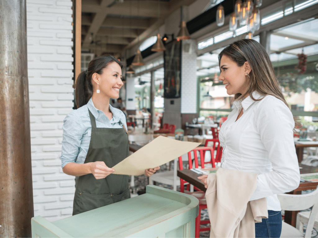 Restaurant host talks with a guest while holding a menu